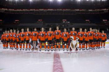 Calgary Hitmen dressed in orange Every Child Matters jerseys stand in a line at centre ice.