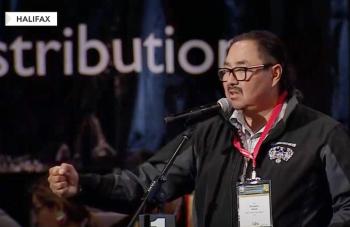 A man at a microphone makes gestures with an outstretched arm and makes a fist.