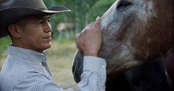A man wearing a cowboy hat rubs the muzzle of a horse.