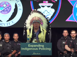 Tsuut’ina Nation Chief Roy Whitney Onespot stands wearing a headdress in from of police members