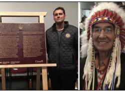 Gabriel Michael stands with plaque. With photo of Wilton Littlechild in a headdress.