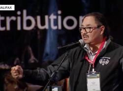 A man at a microphone makes gestures with an outstretched arm and makes a fist.