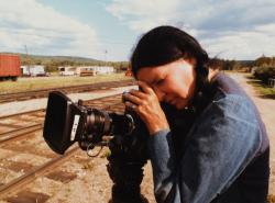A woman sporting a long black braid that hangs over her shoulder stares into a film camera.