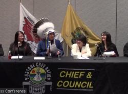A man wearing a feathered headdress sits at a table and is flanked by others.