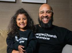 A young smiling girl sits with a smiling bearded man who has his arm around waste.