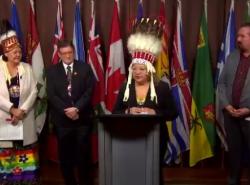 A woman in a chiefs headdress stands at a podium surrounded by other chiefs.