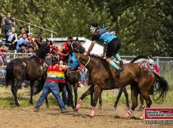 A rider jumps onto a horse to ride bareback around the track. People around him hold back other horses to clear the rider's way.