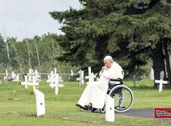 Pope Francis sits in his wheelchair amongst white wooden crosses in a cemetary and prays.